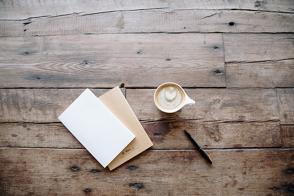 Café, cuadernos y bolígrafo sobre una mesa.