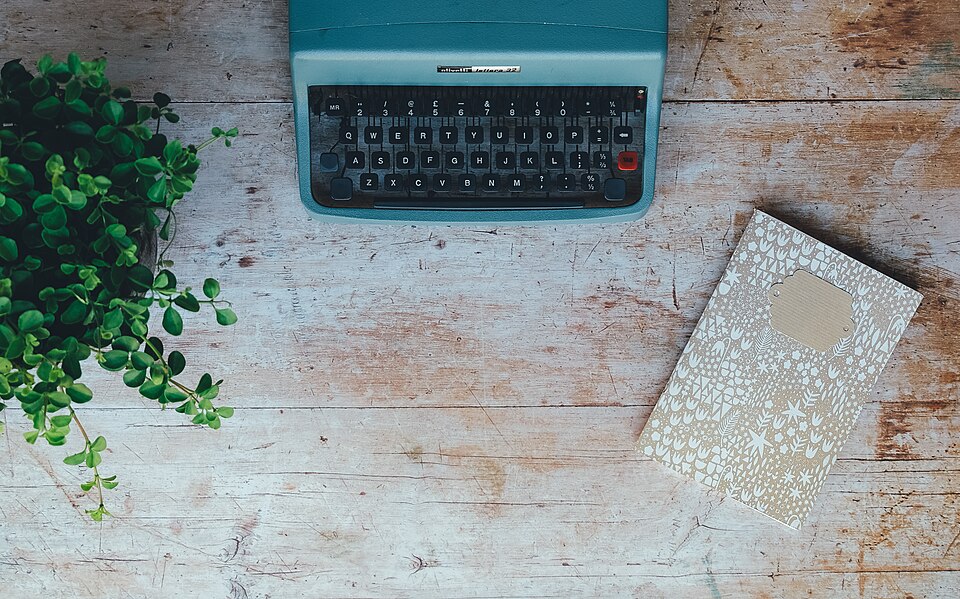 Máquina de escribir, cuaderno y planta sobre una mesa de madera.